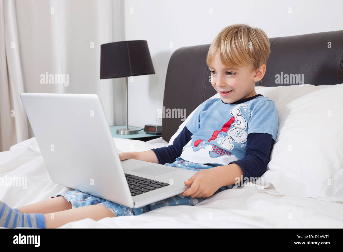 Lächelnd kaukasischen junge mit Laptop-Computer im Bett Stockfoto