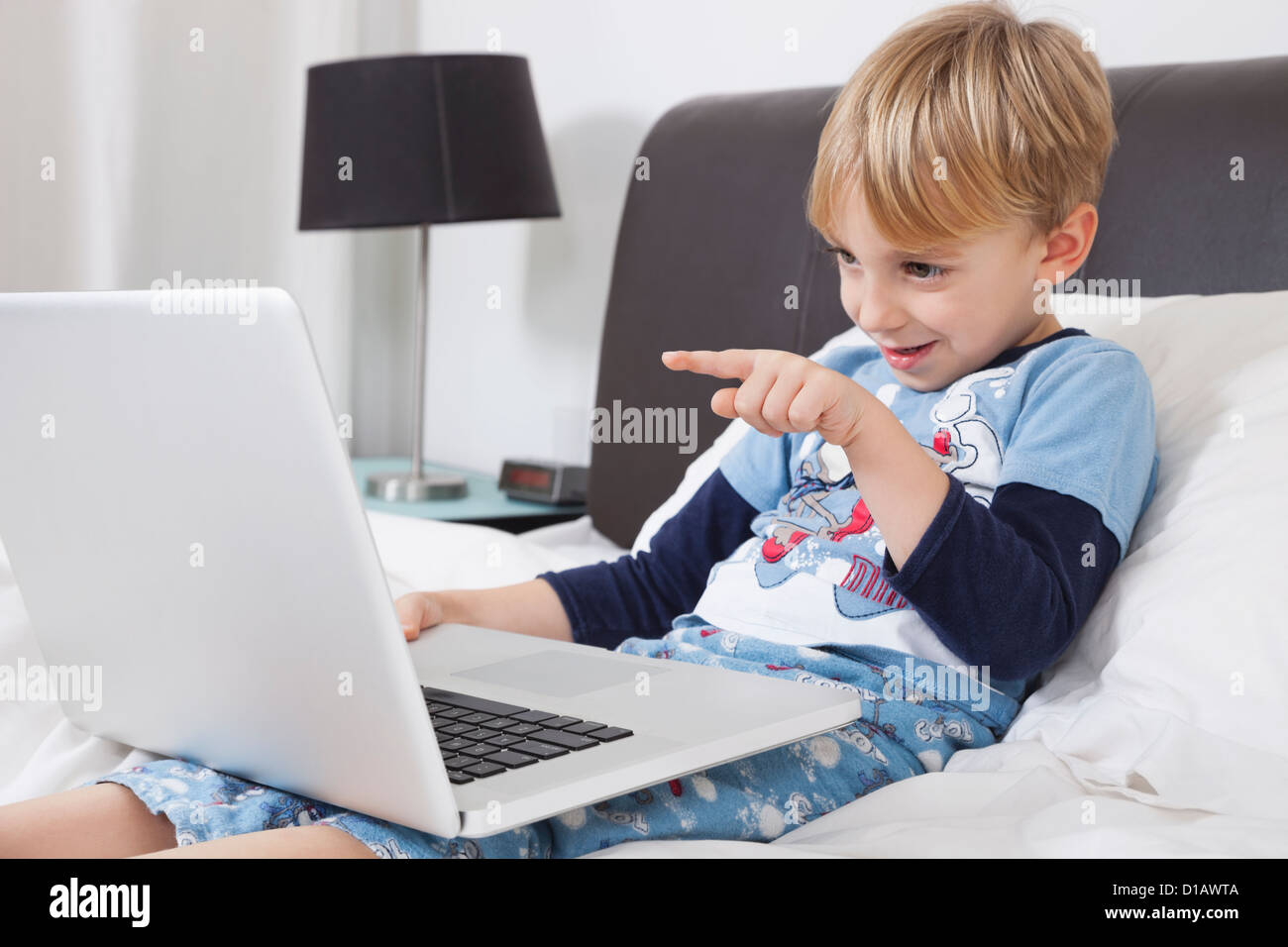 Spielerische kaukasischen junge mit Laptop-Computer im Bett Stockfoto