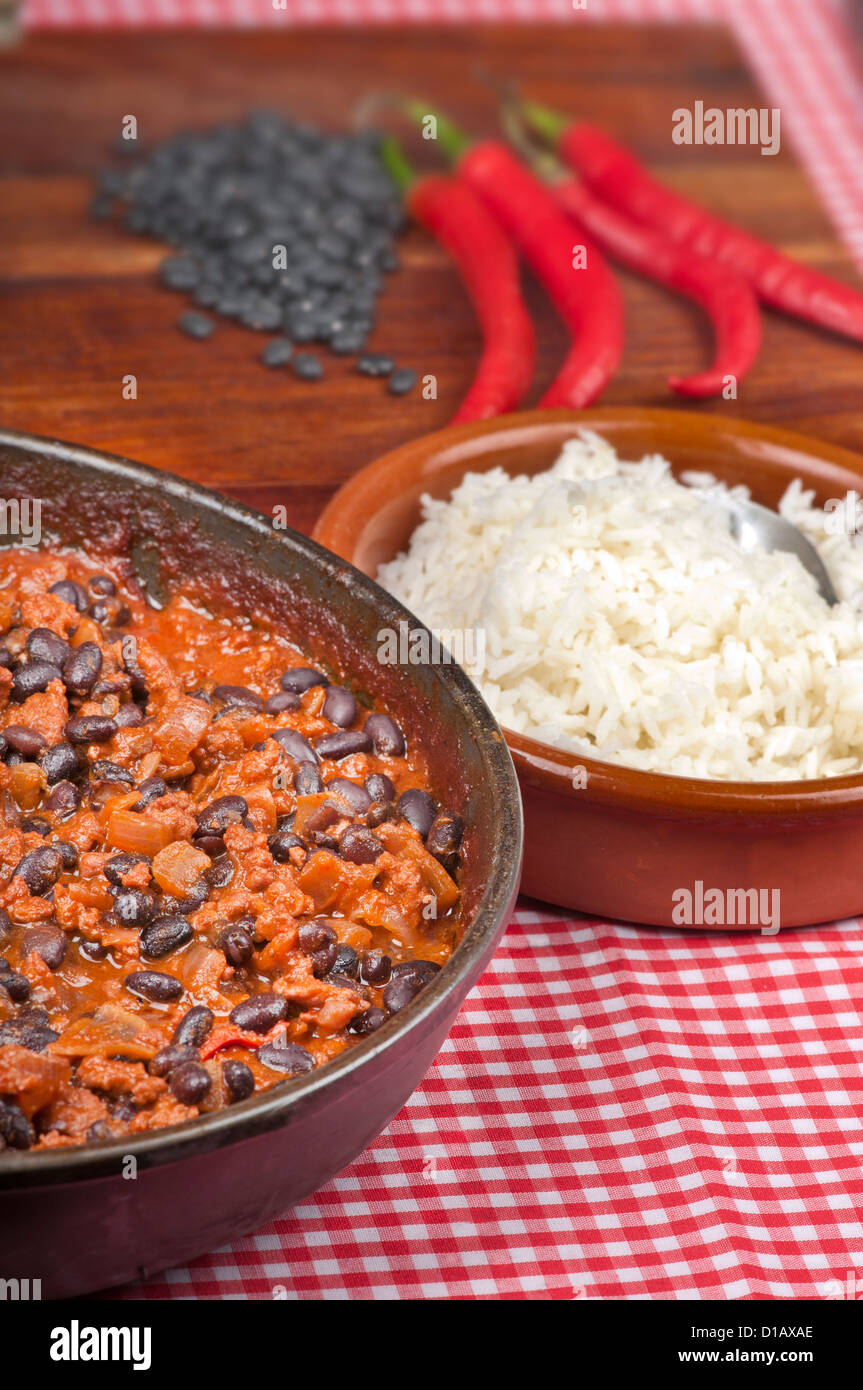 Scharf und würzig Chili Con Carne in der Pfanne mit Reis. Ganze Paprika und schwarzen Rohbohnen im Hintergrund. Stockfoto