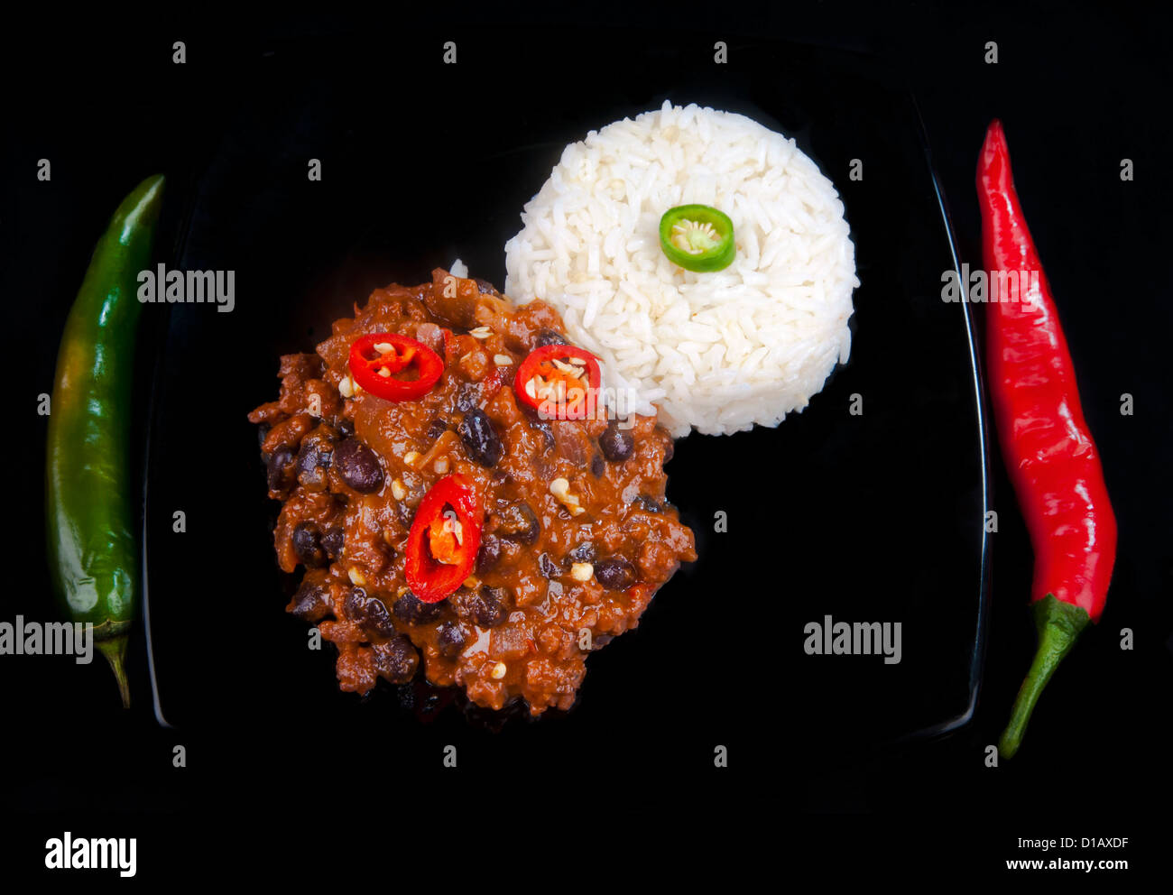 Scharf und würzig Chili Con Carne mit roten und grünen Paprika anstatt mit Messer und Gabel und Reis. Auf einer schwarzen Platte auf schwarz. Stockfoto