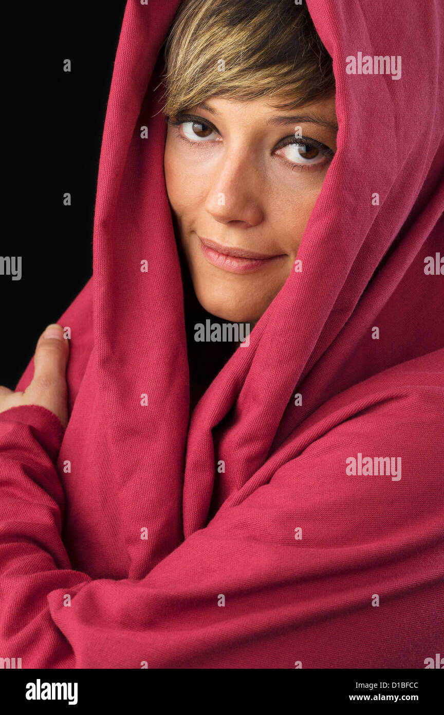 Schöne junge Frau im roten Umhang, freundlich lächelnd und selbstbewusst in die Kamera schauen. Studio erschossen vor einem schwarzen Hintergrund. Stockfoto