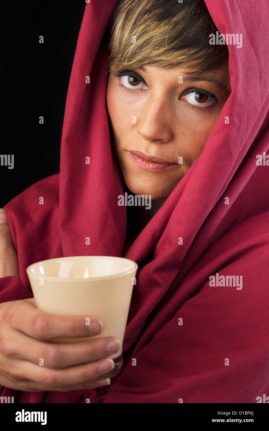 Schön, aber traurig junge Frau im roten Umhang, eine brennende Kerze in ihren Händen hält und nachdenklich in die Kamera schauen. Stockfoto