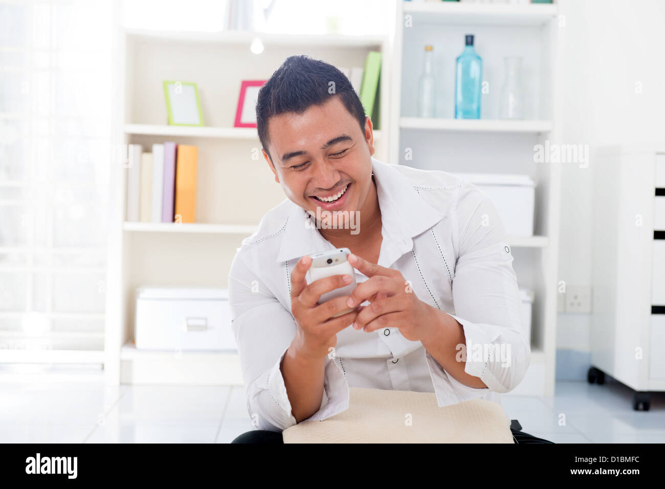 Fröhliche asiatischen Mann mit Smartphone zu Hause, auf der Suche auf dem Bildschirm. Stockfoto