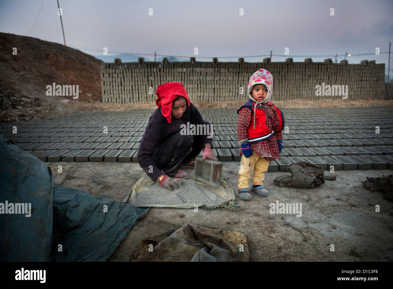 14. Dezember 2012 - Bakthapur, Bakthapur, Nepal - Kumari Manandhar (19) stellen Ziegel während ihr einjähriges Kind durch die Mauer aus Ziegeln in Bakthapur steht. Kinder der Ziegel Arbeitnehmer bleiben oft unbeaufsichtigt, da beide arbeiten... In Nepal gibt es etwa 750 Ziegeleien, während nur 450 mit der Regierung registriert sind. Es gibt 110 Ziegeleien im Kathmandu-Tal während 64 in Bakthapur Bezirk. Keiner von den Fabriken erfüllen Standards des Ministeriums für Industrie für Sicherheit Arbeitsumfeld... 500 Kinder arbeiten in Ziegeleien, die 52 Prozent von ihnen jünger als 10 sind. Öfen mieten Saisonarbeit Stockfoto