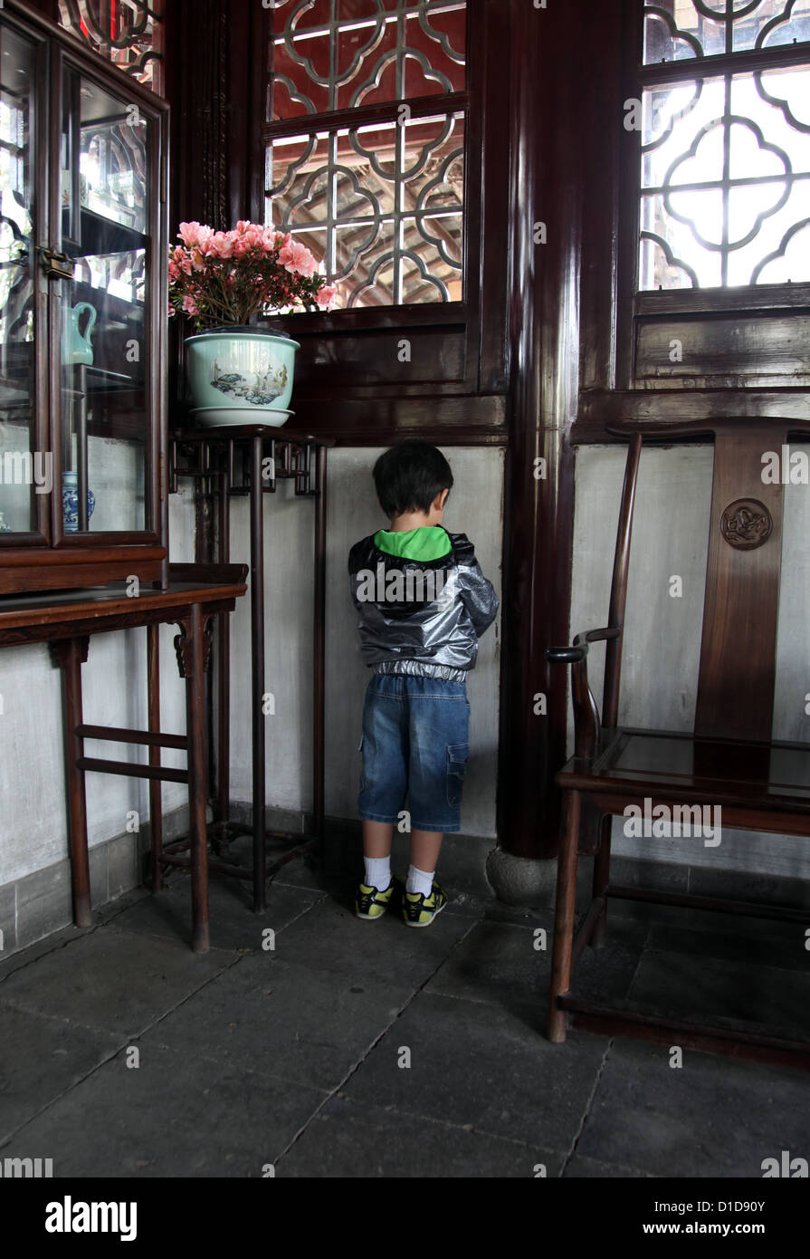 Es ist ein Foto einer kleinen Jungen-Ansicht von hinten, in der Ecke eines Raumes im chinesischen Stil zu bestrafen ist. Er trage keine Esels Hut Stockfoto