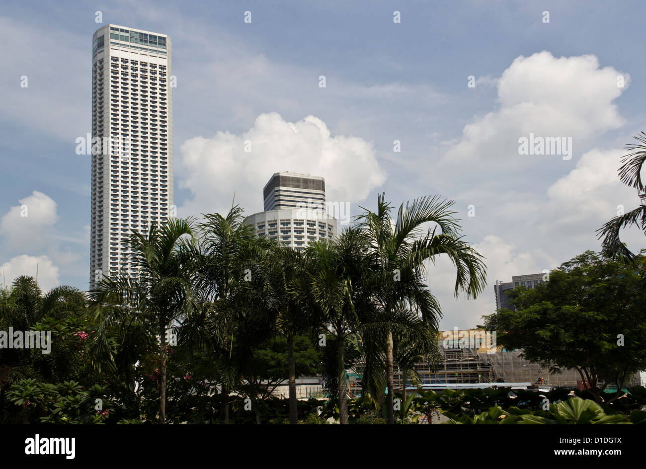 Hochhäuser hinter Bäumen neben dem Bau zu arbeiten, in Singapur, inmitten ein blauer Himmel mit weißen Wolken steigen Stockfoto