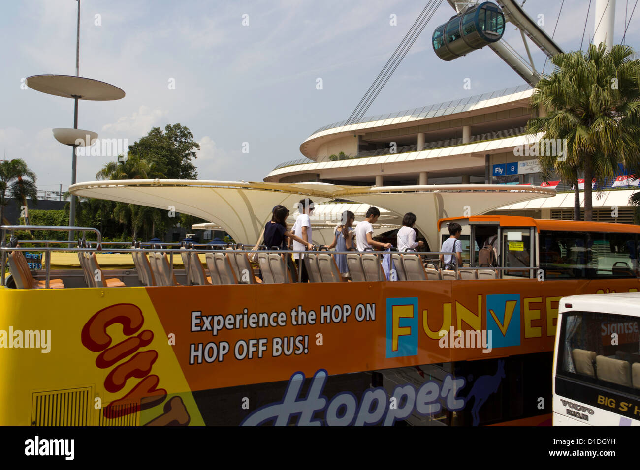 Singapur-Sightseeing-Bus an der Basis der Singapore Flyer, mit Touristen, die nach unten aus dem teilweise offenen Oberdeck des Busses Stockfoto