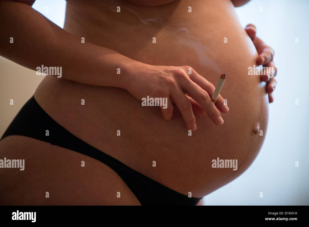 Ein undatiertes symbolisches Bild zeigt eine schwangere Frau eine brennende Zigarette in der rechten Hand hält, und ihren Bauch mit dem linken Abschirmung. Foto: Hans Wiedl - Modell veröffentlicht Stockfoto