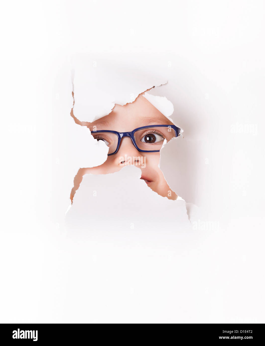 Neugierige Kind in Brille schaut durch ein Loch im Weißbuch Stockfoto
