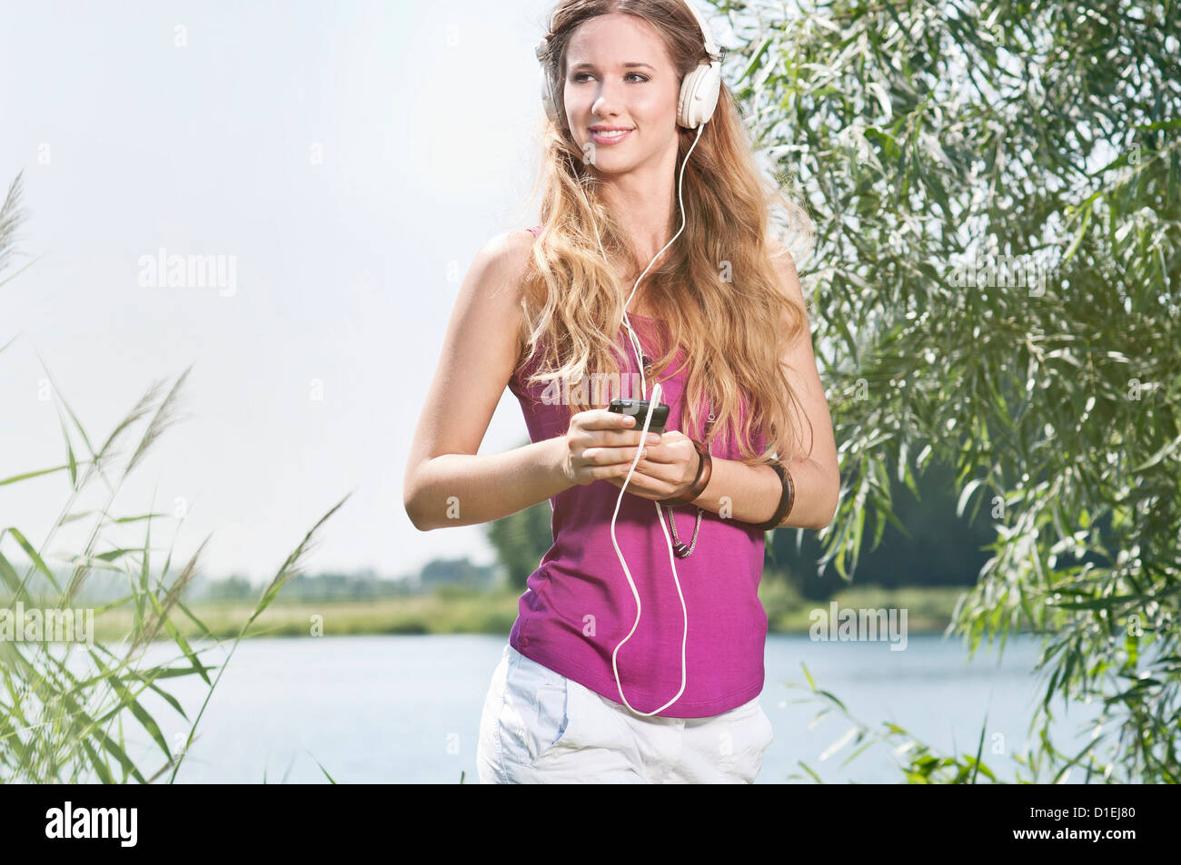 Blonde junge Frau anhören von Musik am See Stockfoto