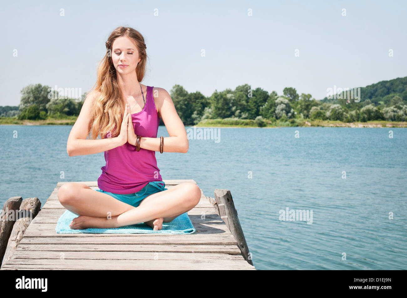 Blonde junge Frau praktizieren Yoga am See Stockfoto