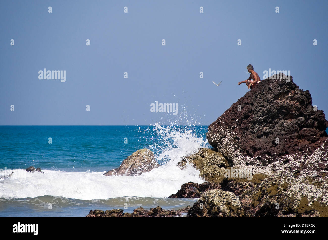 Horizontale Ansicht eines indischen Mannes thront prekär auf ein Rock-Fischen am Papanasam Beach in Varkala, Kerala. Stockfoto