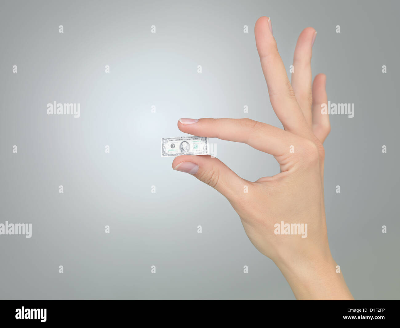 weibliche Hand hält einen kleinen Geldschein auf grauem Farbverlauf Hintergrund Stockfoto