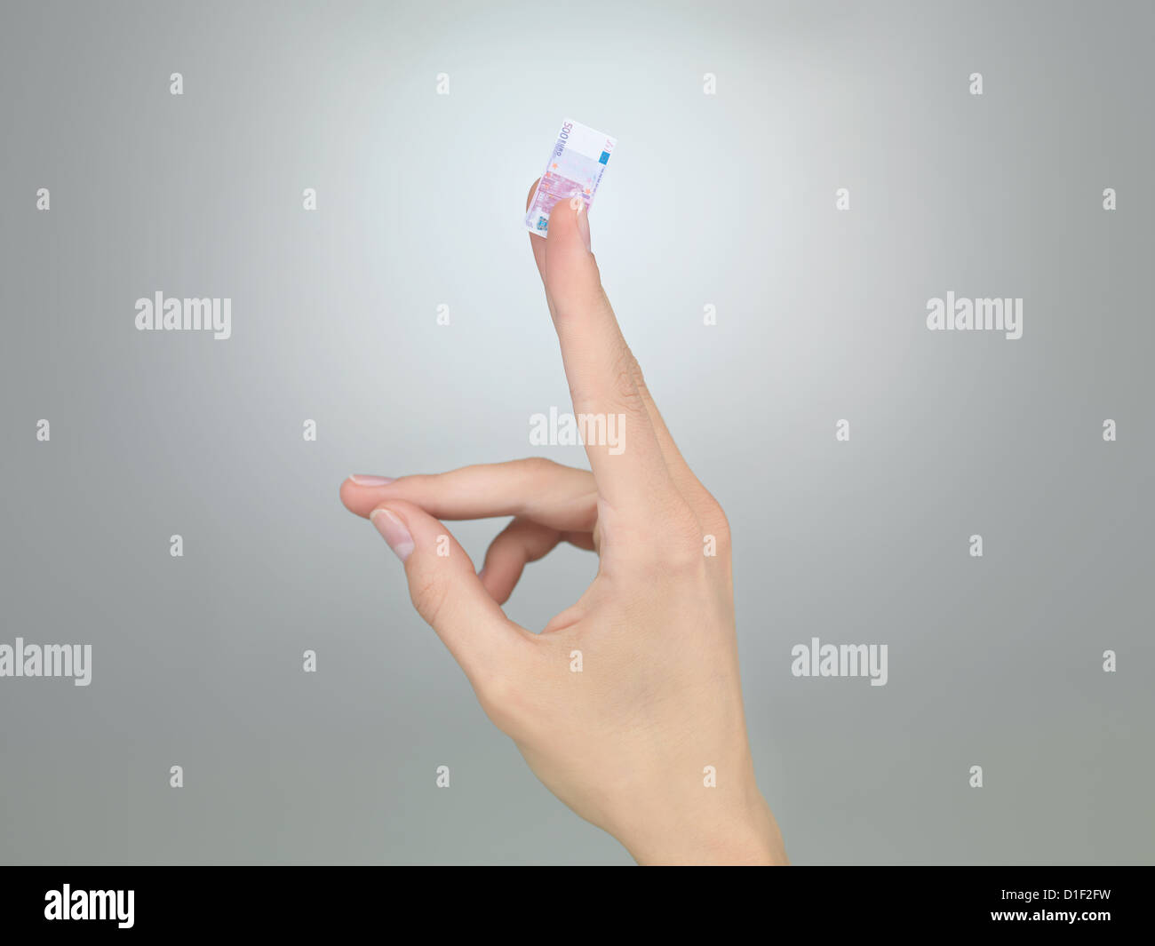 weibliche Hand halten eine winzige fünfhundert Euro Rechnung zwischen zwei Fingern auf grauem Farbverlauf Hintergrund Stockfoto