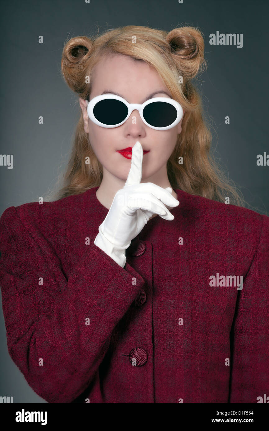 eine Frau in einem Vintage Blazer mit Vintage Sonnenbrillen im 50er Jahre Stil mit dem Finger auf den Lippen Stockfoto
