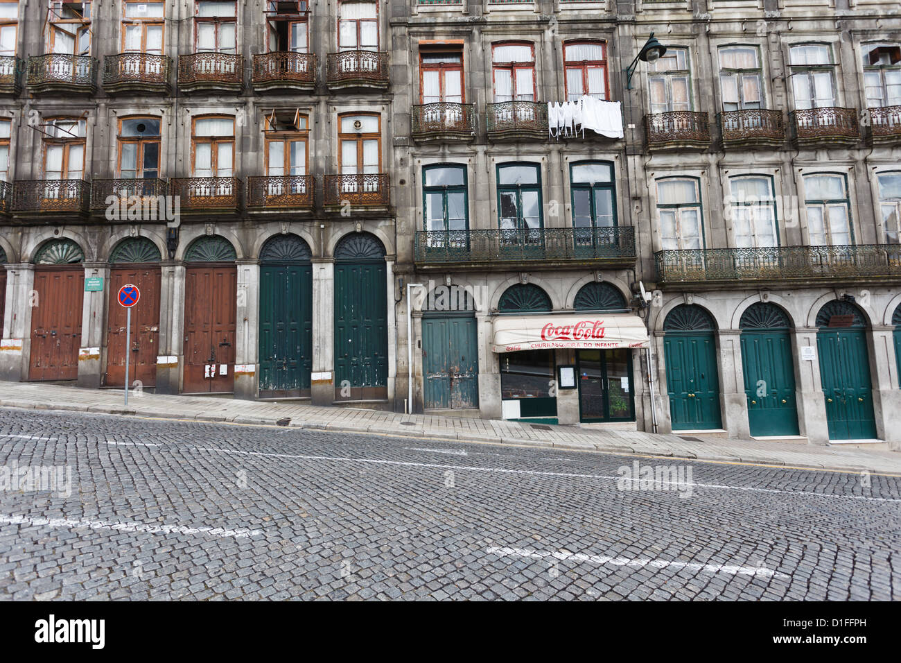 Fassade der unteren Geschosse eines Apartmenthauses in einer steil abfallenden Kopfsteinpflasterstraße in Porto Portgal. Die Fenster und Türen ändern sich in Größe und Höhe, wenn man die Straße hinunter fährt. Stockfoto
