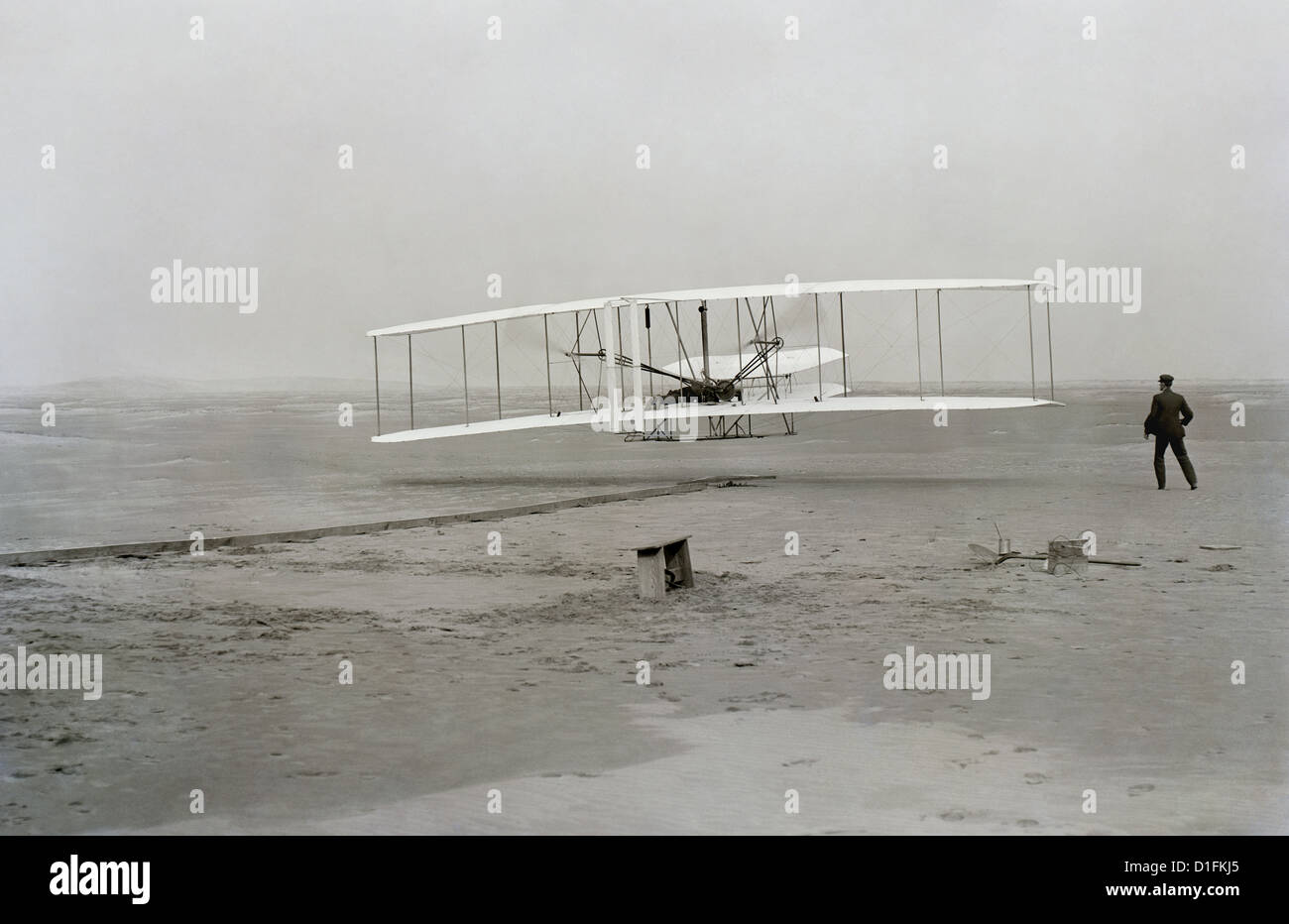 Ersten erfolgreichen Flug der Wright Flyer der Gebrüder Wright. Die Maschine reiste 120 ft in 12 Sekunden bei 10:35 in Kitty Hawk, North Carolina. Orville Wright wurde an der Steuerung der Maschine, Bauchlage auf der unteren Tragfläche mit den Hüften in die Wiege, die den Flügel-verwerfen Mechanismus betrieben. Wilbur Wright lief neben die Maschine auszugleichen, und hat soeben seinen Einfluss auf die vorwärts aufrechte des rechten Flügels auf dem Foto. Der Start Schiene, Flügel-Rest, eine Spule-Box und andere Gegenstände benötigt zur Flugvorbereitung sind sichtbar hinter der Maschine. Dies war die erste Sust betrachtet. Stockfoto