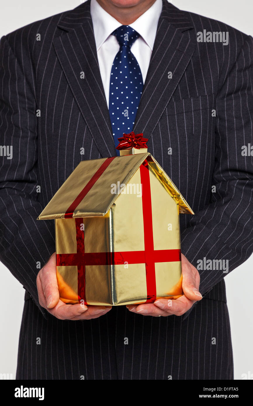 Ein Geschäftsmann präsentiert ein neues zu Hause Geschenk verpackt in Goldpapier mit Band und Schleife. Gutes Bild für Hauskauf bezogene Themen. Stockfoto