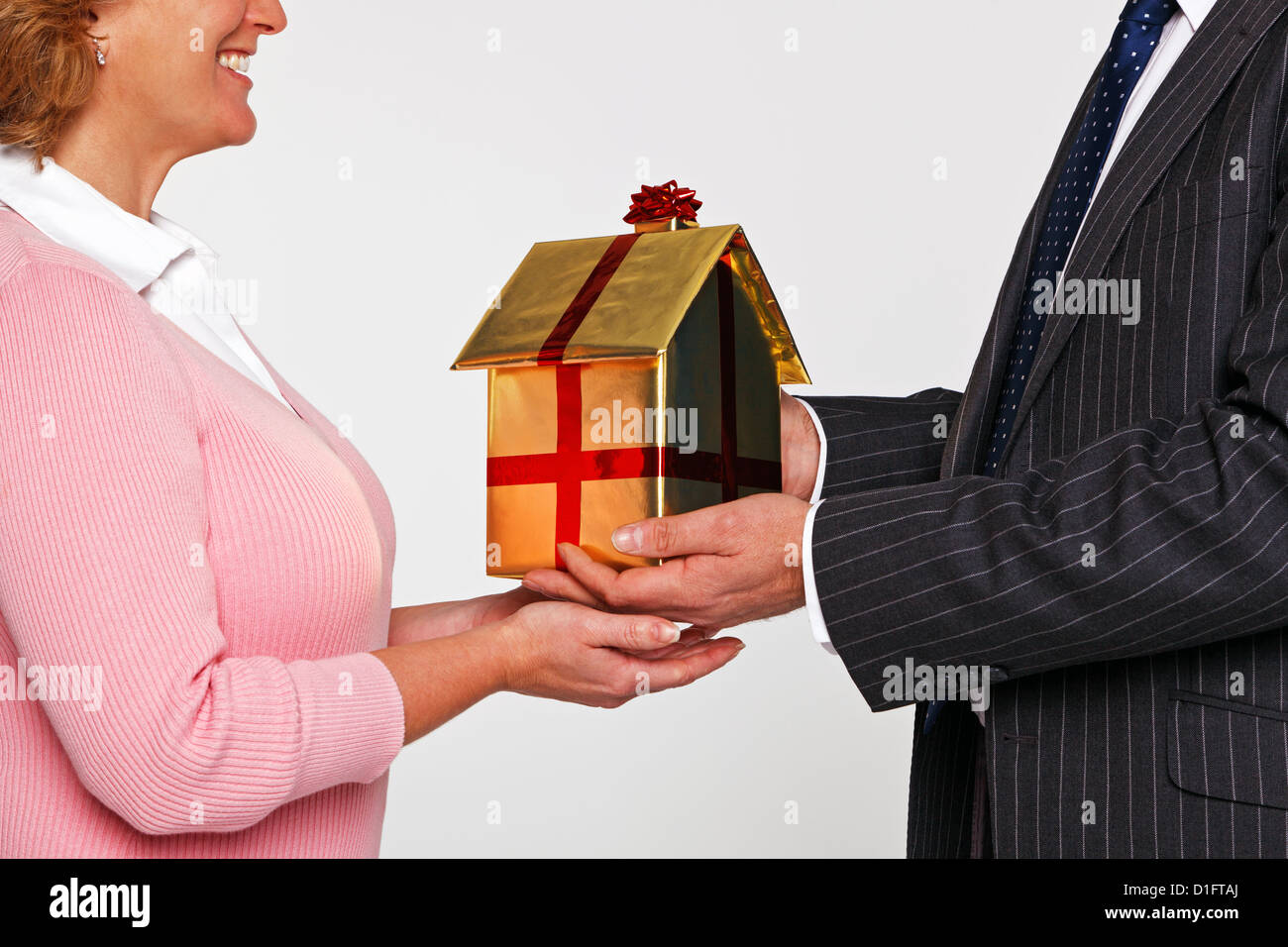Ein Geschäftsmann, so dass eine Frau ein neues Zuhause in Goldpapier mit rotem Band und Bogen gewickelt. Gutes Bild für Haus Kauf Themen. Stockfoto