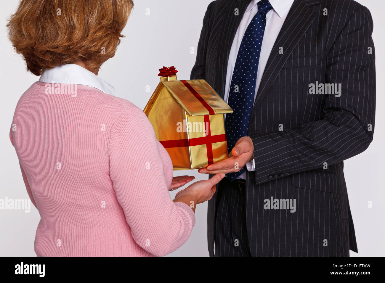 Ein Geschäftsmann Übergabe ein neues Zuhause in Goldpapier mit rotem Band und Bogen zu einer Frau in Freizeitkleidung gewickelt. Stockfoto