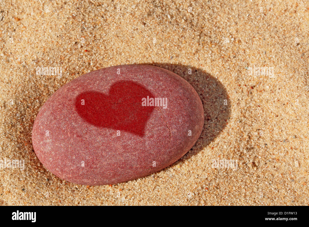 Der rote Kiesel am Strand mit einer nassen Herzform darauf. Stockfoto