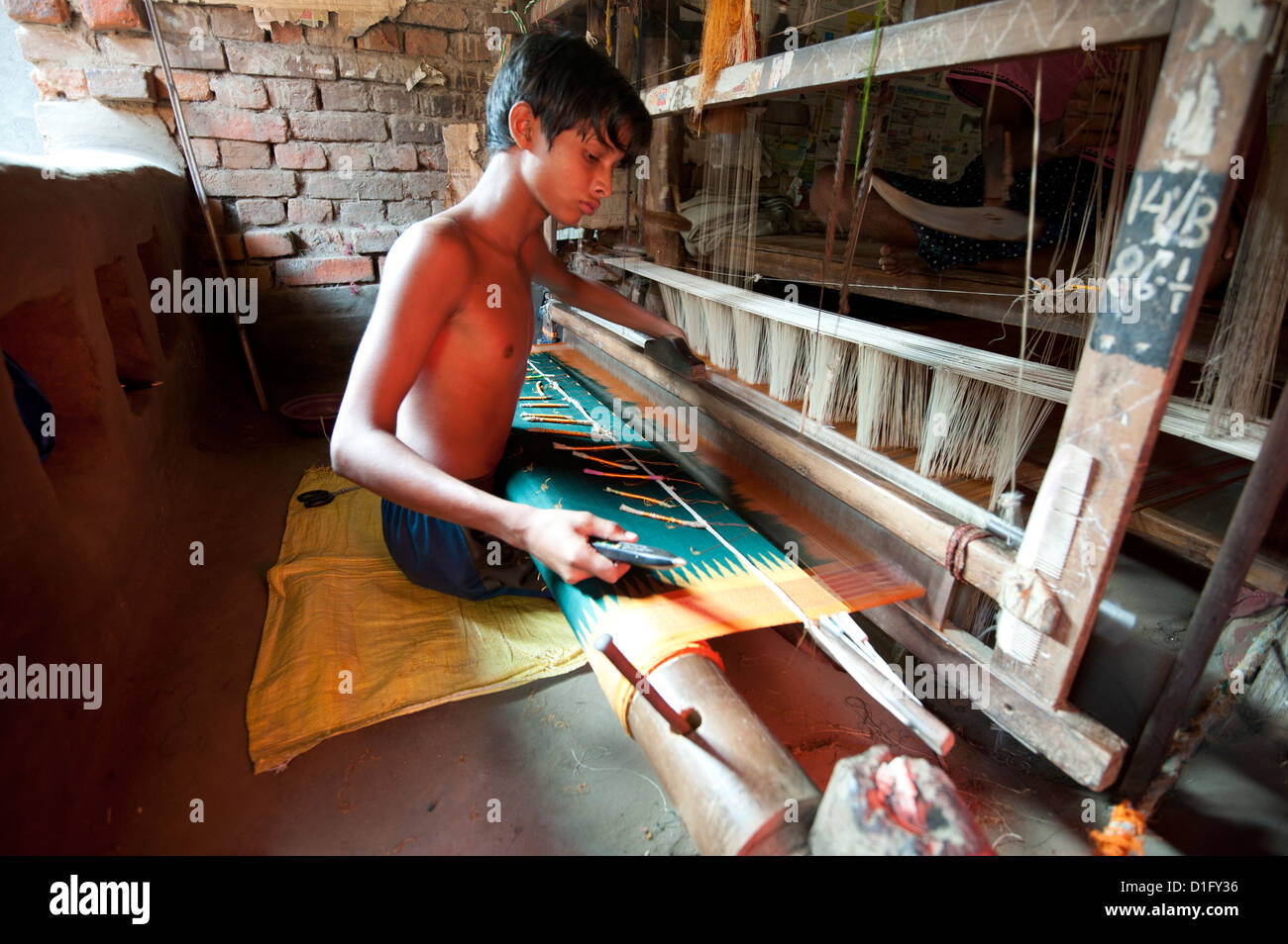 Kleiner Junge am Webstuhl weben gemusterte Seide Sari mit mehreren Spulen von Seide, Vaidyanathpur weben Dorf, Orissa, Indien Stockfoto