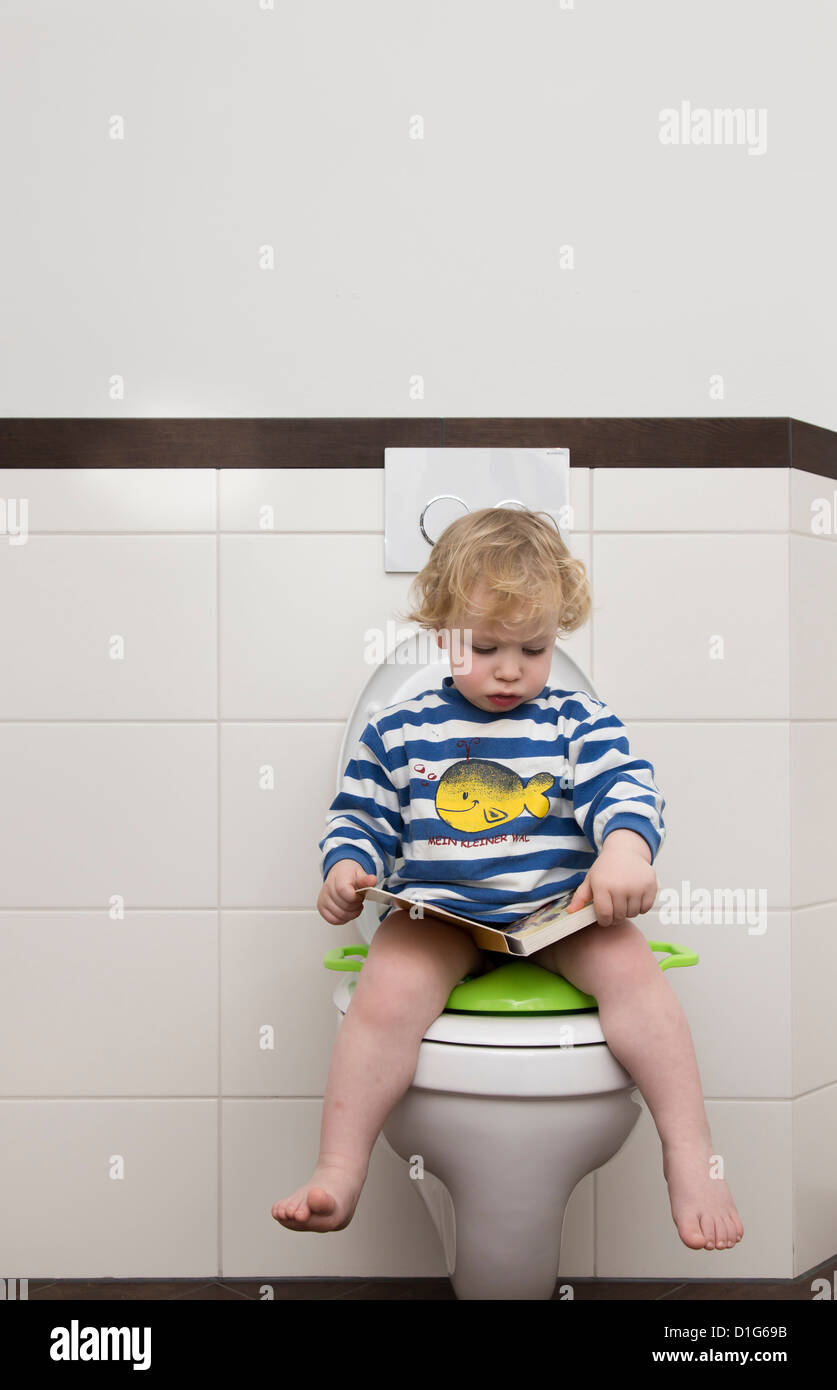 Junge, 2 Jahre alt, sitzt auf einem Kindersitz auf einer Toilette. Stockfoto