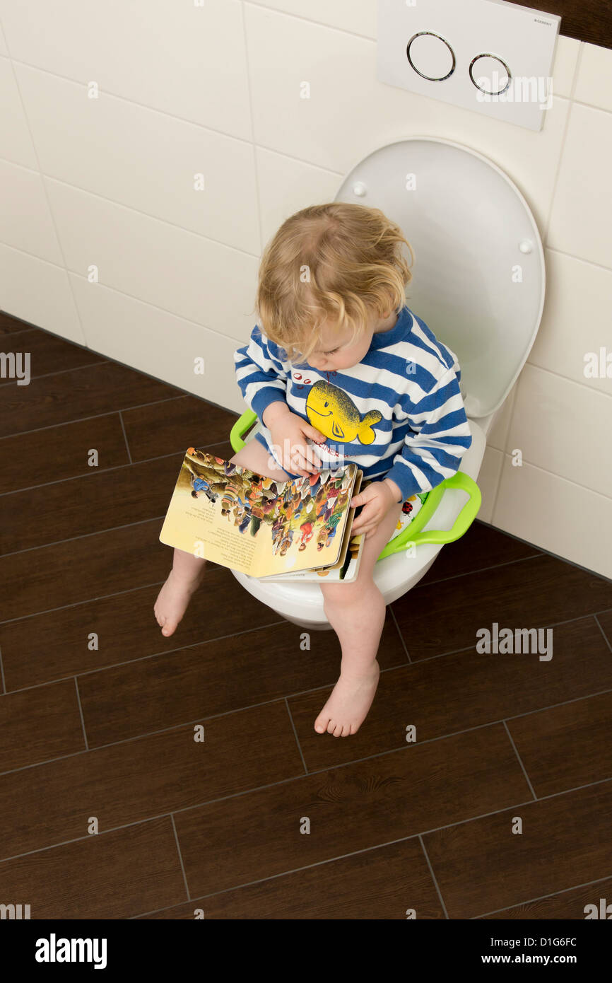 Junge, 2 Jahre alt, sitzt auf einem Kindersitz auf einer Toilette. Stockfoto