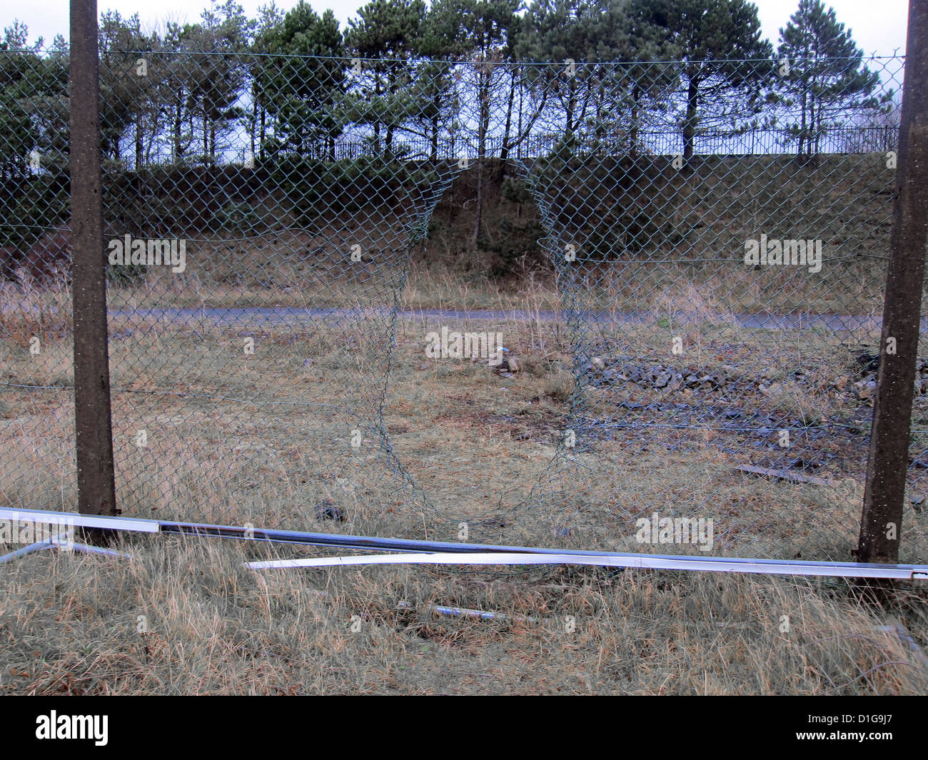 Loch gebildet in ein beschädigtes Kabel Sicherheitszaun rund um ein leeres Grundstück, in der Nähe von Swansea, Südwales, Dezember 2012 Stockfoto