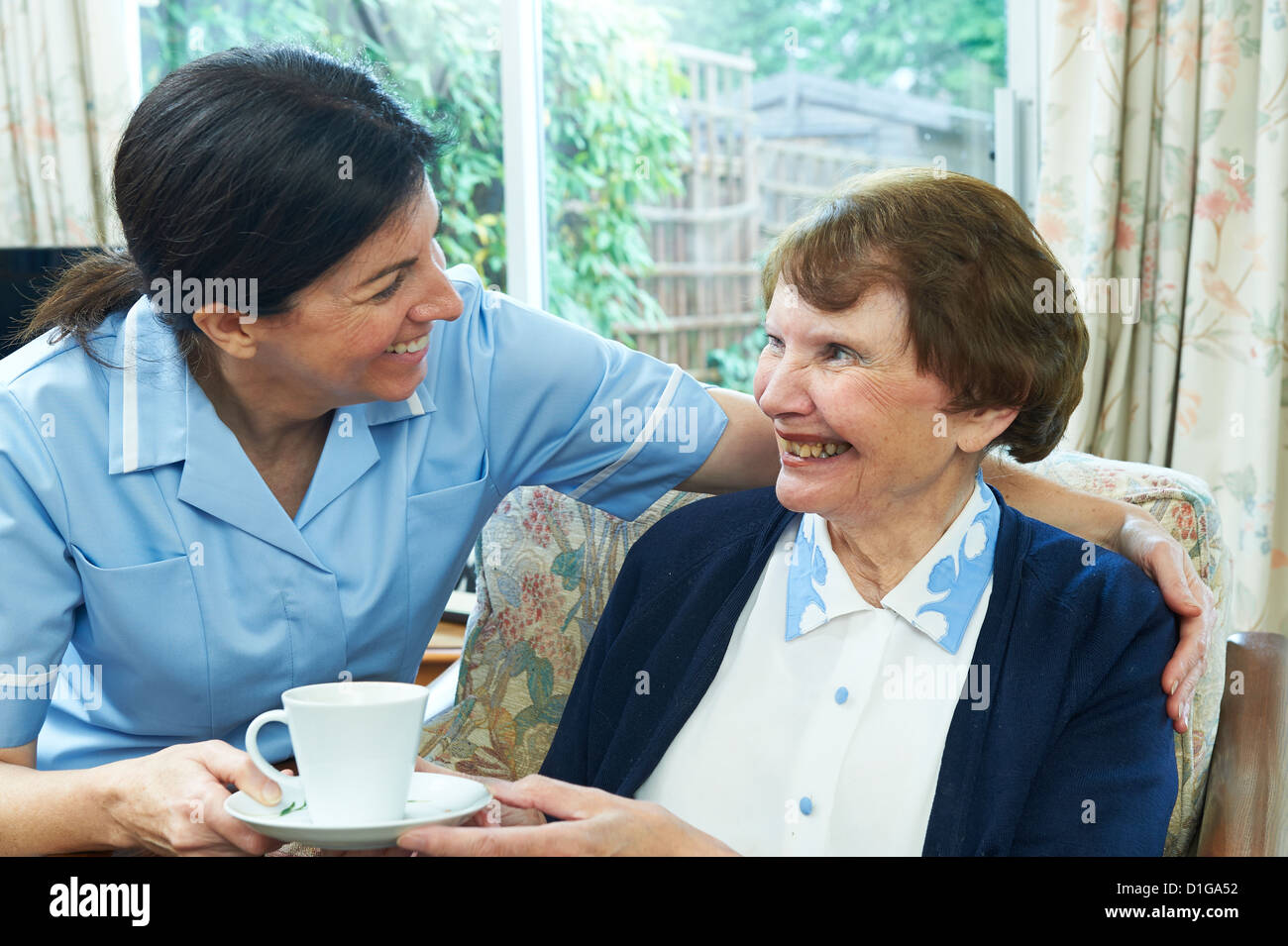 Attraktive Gesundheitswesen Arbeitnehmerin einer älteren Frau zu geben, eine Tasse Tee zu Hause Stockfoto