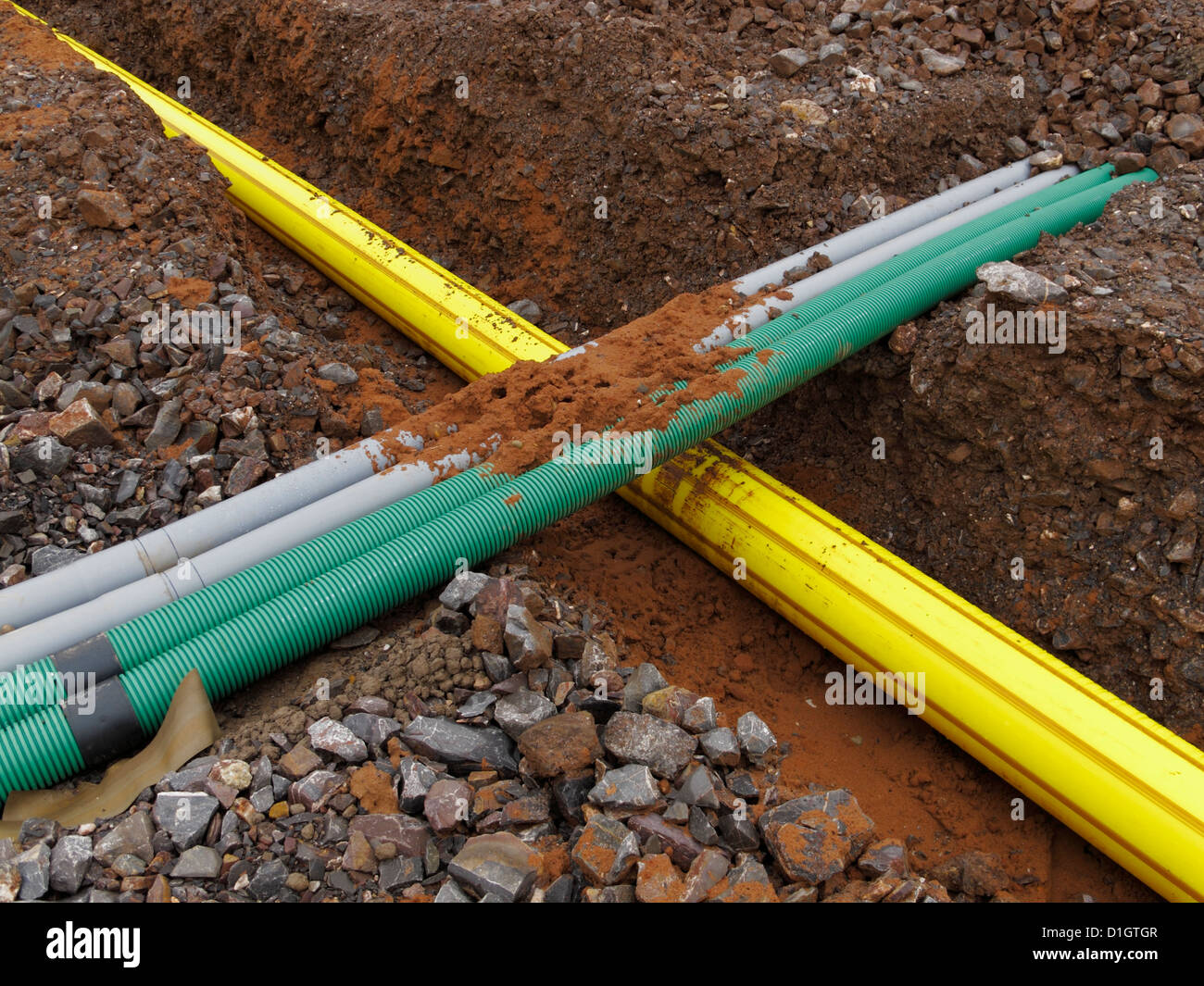 Neue gelbe Hochdruck-Gasleitung in einem Graben durchzogen von grauer und grüner unterirdische Leitungen für elektrische Verkabelung UK Stockfoto