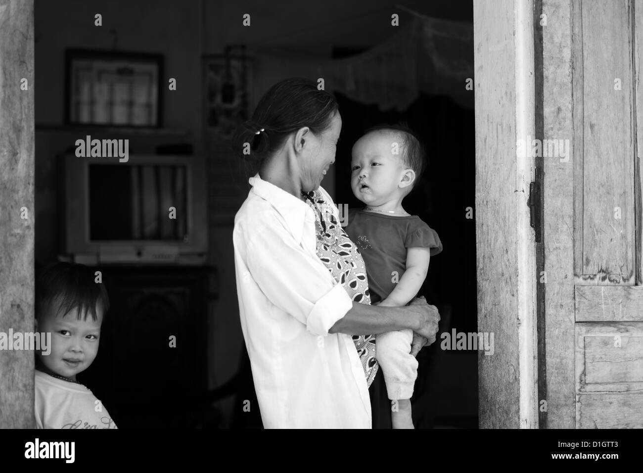 Großmutter blickt liebevoll auf Enkel, während andere Geschwister blickt auf. Aufgenommen in Kenh Ga Fischerdorf in Ninh Binh Stockfoto