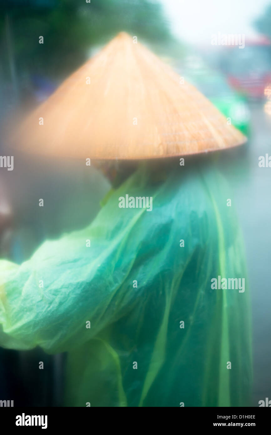 Vietnamesische Arbeiter in Bambushut und arbeiten in einem Sturm Regen Poncho. Stockfoto