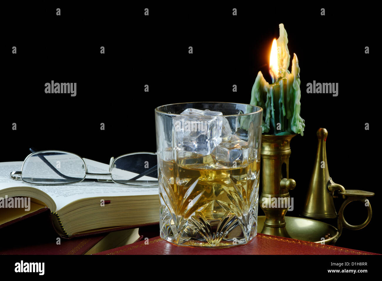 Ein Glas Whisky mit Eis auf ein antikes Buch mit Kerze und Gläser stehen Stockfoto
