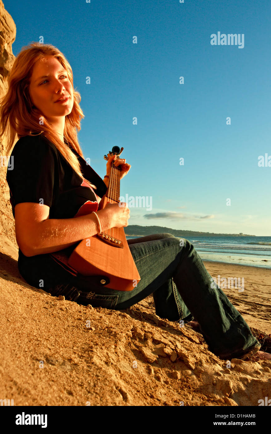 Eine schöne junge Frau wird erfasst, am Strand, beim Gitarre spielen. Stockfoto