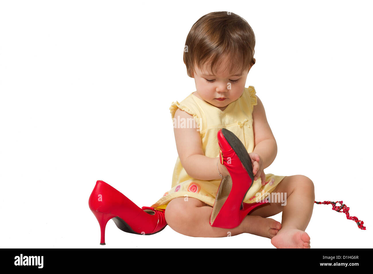 kleines Mädchen versucht auf Mutter s großen roten Schuhen auf weißem Hintergrund Stockfoto