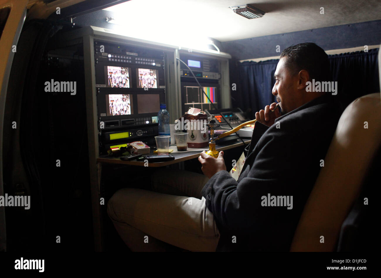 Ein Techniker des palästinensischen Fernsehsenders Shisha Pfeife rauchen, wie er beobachten ein Weihnachtsfest Masse übertragen in eine Kontrolle Handy News van in Bethlehem Israel Stockfoto