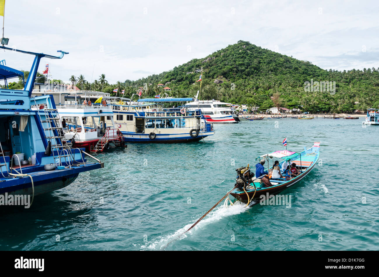 Touristischen Longtailboot geht durch größere verankerte Boote im Hafen von Ban Mae Hat auf Koh Tao im Golf von Thailand Stockfoto