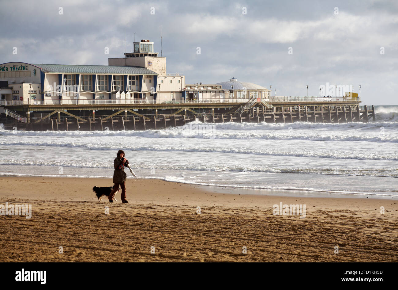 Frau nehmen Hund für einen Spaziergang am Strand von Bournemouth am Weihnachtstag mit Bournemouth Pier hinter Stockfoto