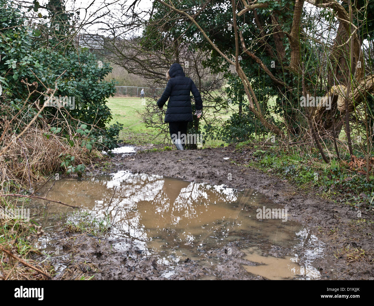 Eine Frau versucht, ihren Weg um eine schlammige Pfütze im Winter Regen machen eingewickelt. Stockfoto