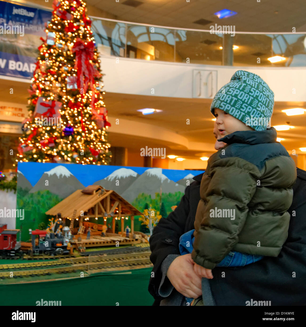 26. Dezember 2012 - Garden City, New York, USA - The Long Island Garden Railway Society großen Zug Modelldarstellung umgibt einen großen geschmückten Weihnachtsbaum für eine festliche Winter Urlaub Attraktion im großen 3-stöckigen Atrium des Cradle of Aviation Museum. Dieser junge, der mit seiner Familie kam, ist vor ein Modell der Sägemühle, die Blaupausen von einem tatsächlichen Sägewerk ein LIGRS Mitglied hergestellt herunterskaliert. LIGRS teilt wissen, Spaß und Kameradschaft der groß angelegten railroading sowohl im Innenbereich als auch im Garten und Familie orientiert. Stockfoto