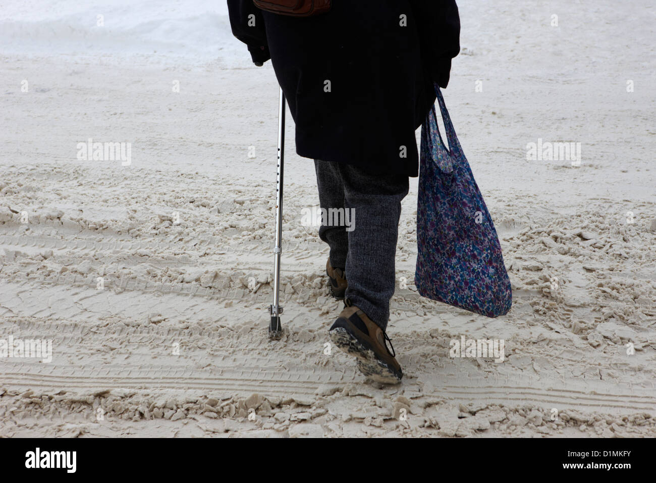 Frau mit Krücke gehen auf Schnee bedeckt Straße Saskatoon Saskatchewan Kanada Stockfoto