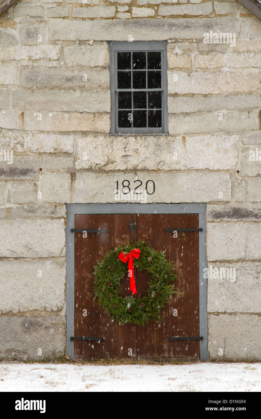 Weihnachten Kranz schmückt eine hölzerne Tür eine alte Scheune in einem Weihnachten Szene mit fallendem Schnee New England. Stockfoto