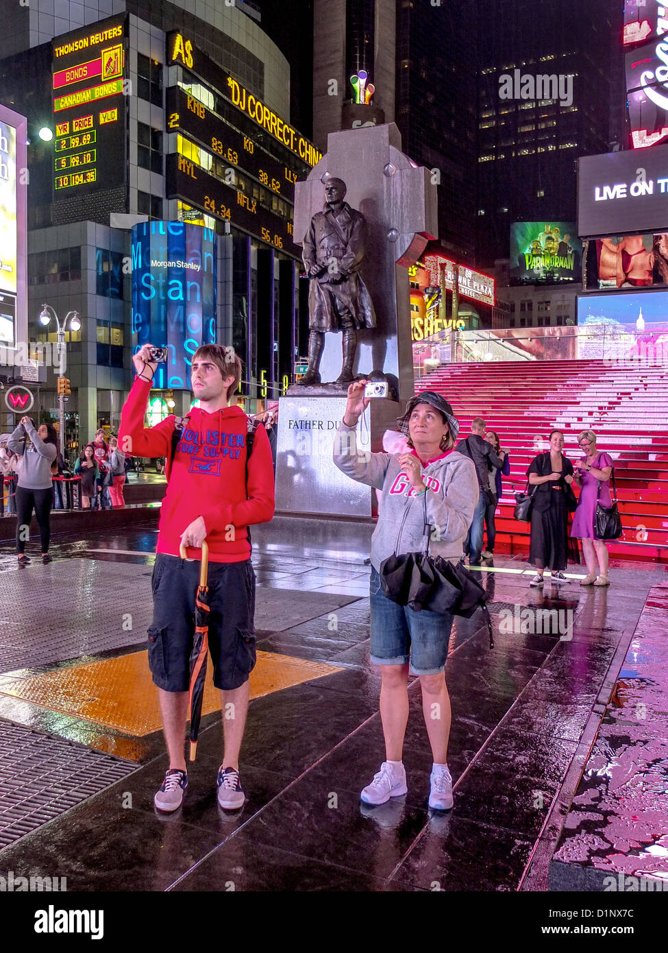 Mit Smartphone-Kameras, fotografieren zwei junge Erwachsene Touristen Times Square in New York City an einem regnerischen Abend. Stockfoto