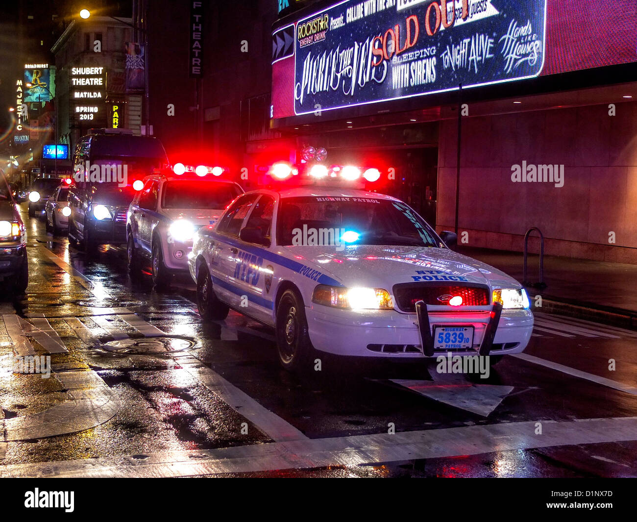 Ein Polizei-Auto-Autokorso begleitet eine Limousine in New York City Times Square Theaterviertel an einem regnerischen Abend. Stockfoto