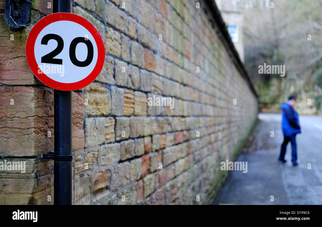 20 mph Höchstgeschwindigkeit Zeichen an der Seite von einer Steinmauer mit einem Mann zu Fuß entfernt, im Hintergrund. Stockfoto