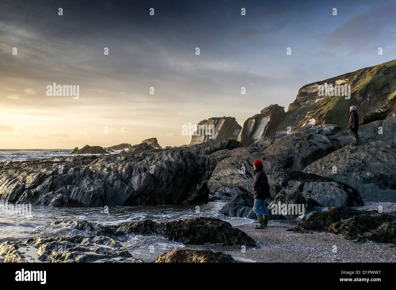 Ein Paar beobachtet vom Strand aus die Wintersonne, die über das Meer untergeht. Ayrmer Cove, Devon. GROSSBRITANNIEN Stockfoto