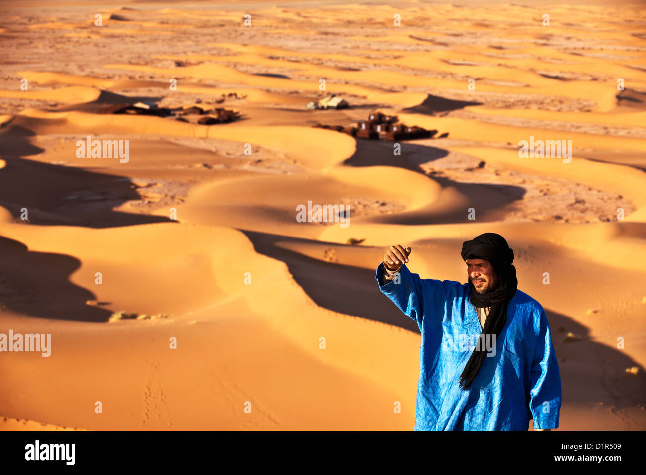 Marokko, M' Hamid, Erg Chigaga Dünen. Wüste Sahara. Lokalen Berber Mann auf Sanddüne, Hintergrund Touristenlager, Biwak. Stockfoto