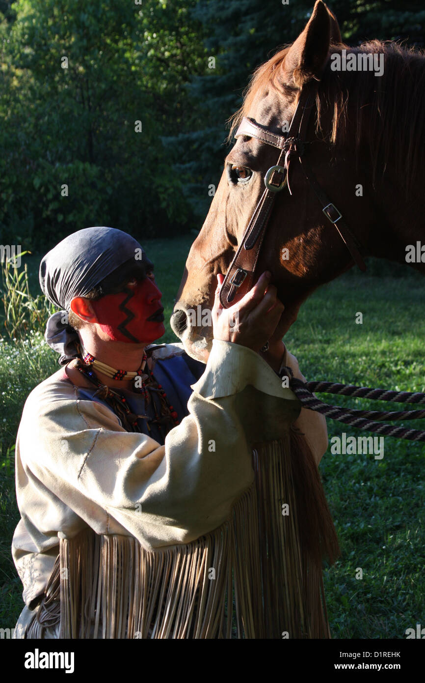 Ein Native American Indian Mann mit roter Bemalung blickte zu seinem Pferd. Stockfoto