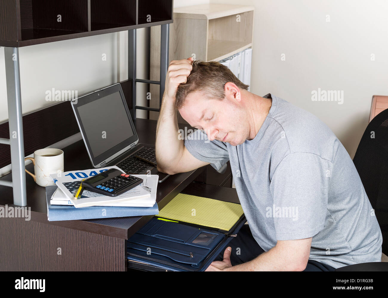 Reifen Mann Kopf in der hand haltend, mit Computer, steuerliche Einkommen Booklet und Kaffee Tasse auf Schreibtisch Stockfoto